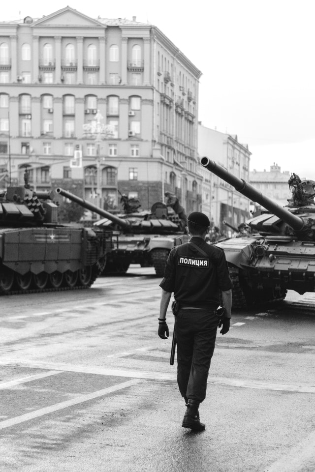 A man walking down the street in front of tanks.