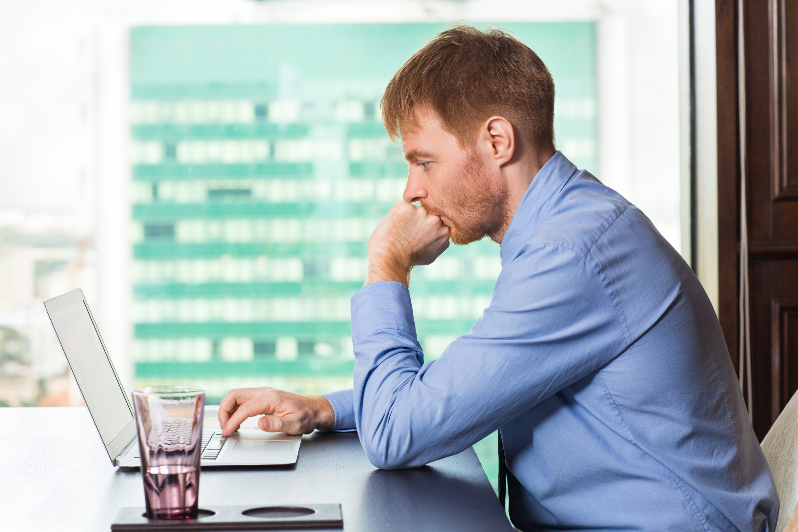 A man sitting at a table with his hand on the keyboard of a laptop.