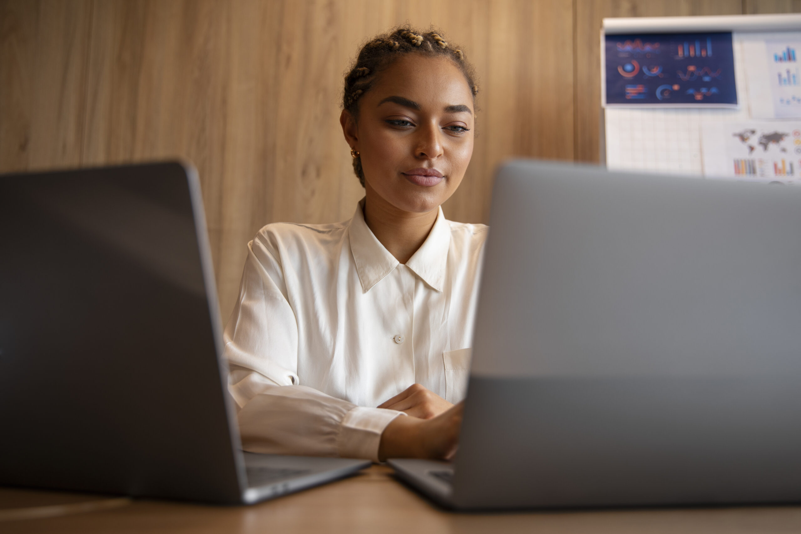 A woman sitting at a table with two laptops.