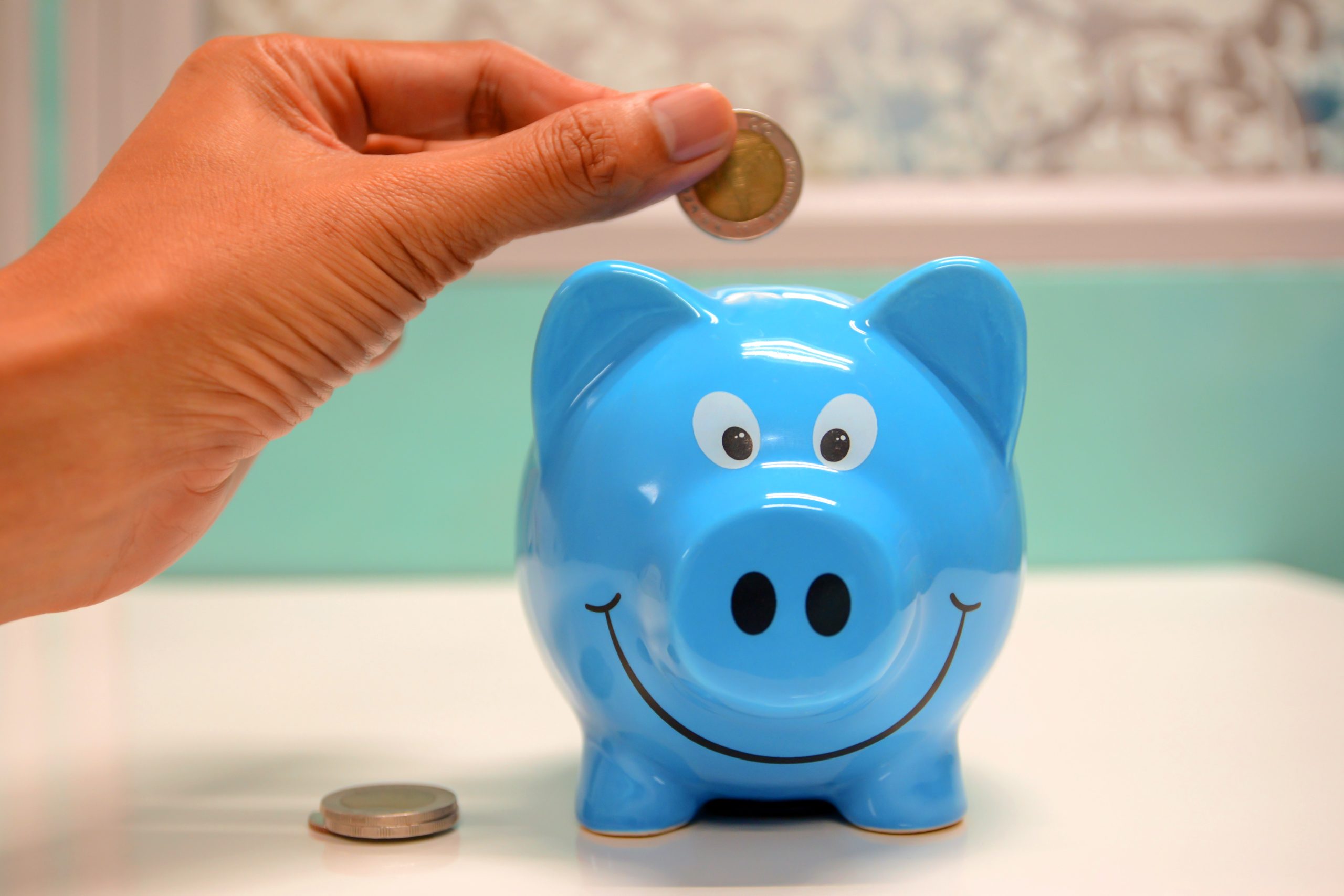 A person putting money in to a blue piggy bank.